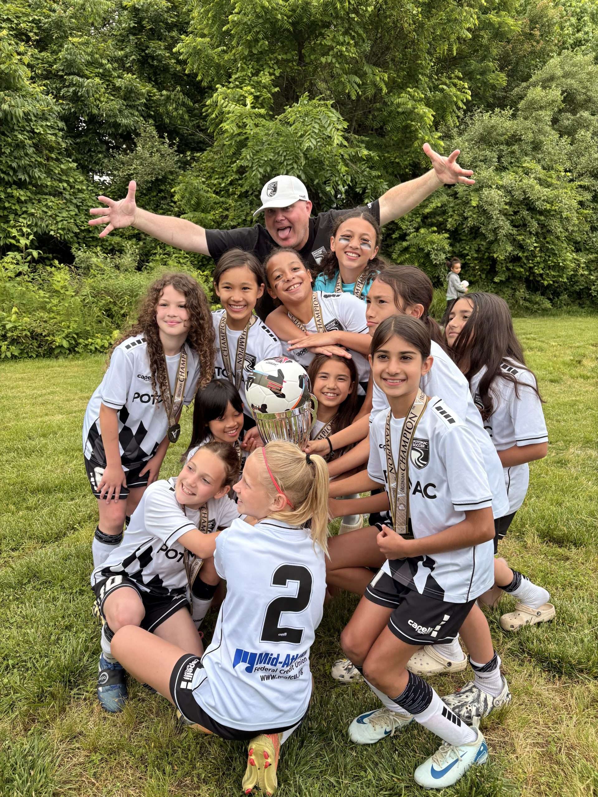 team photo of U12 girls and their coach on a soccer field holding a trophy